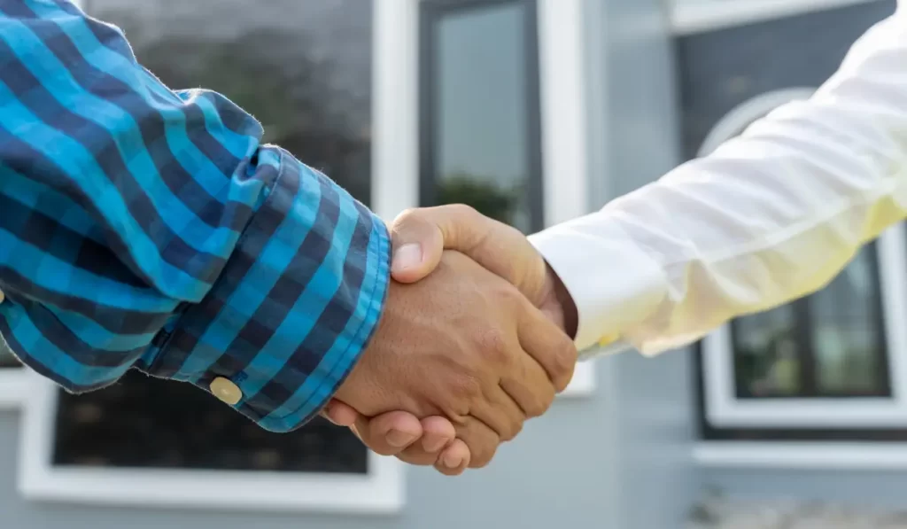 Close-up of handshake in front of house, showing trust in full-service property management partnership agreement.